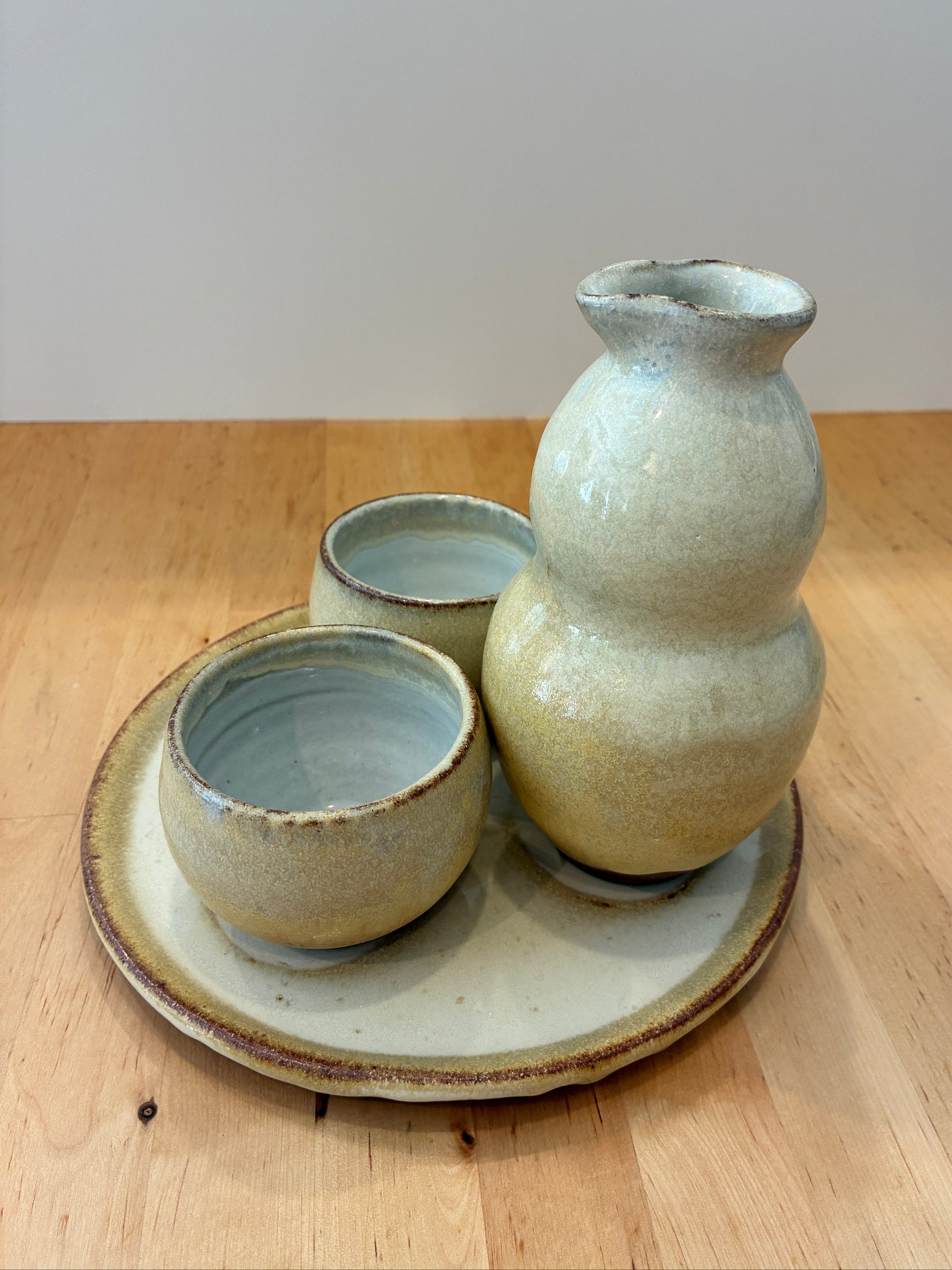 Set of ceramic items including a vase and two cups on a wooden surface.